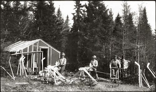 Old black-and-white photo of people carving hockey sticks outside a workshop