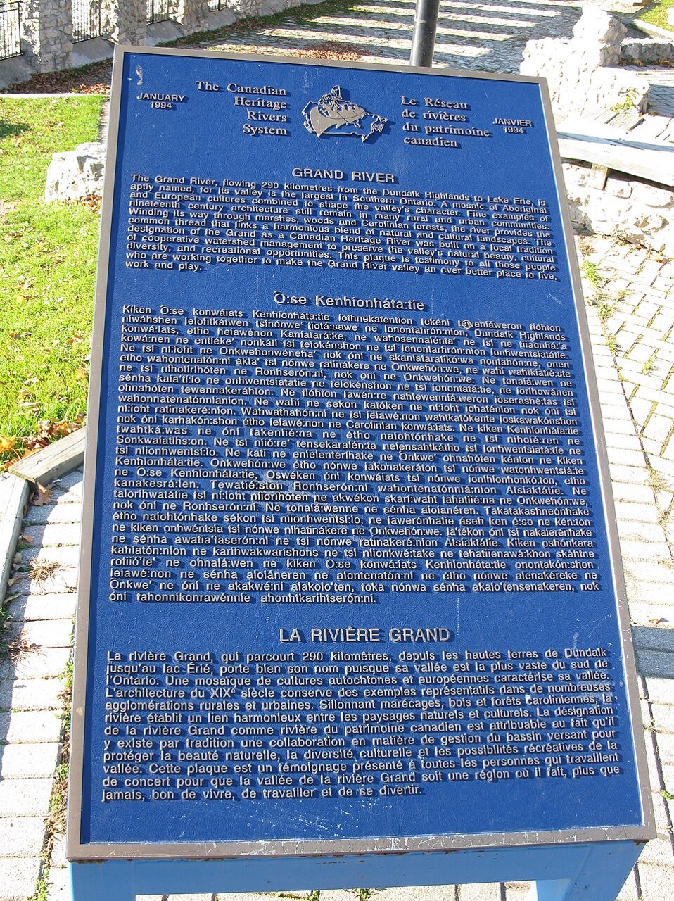 Blue Canadian Heritage River plaque beside the Grand River, written in three languages