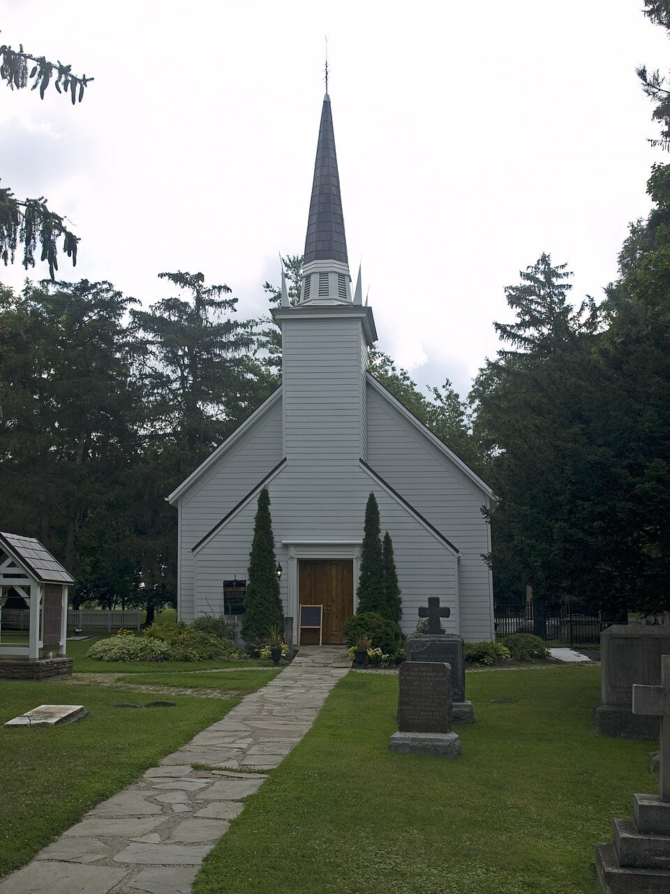 Small white wooden chapel with a tall steeple, surrounded by trees and gravestones